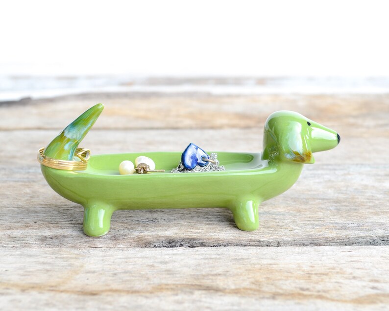 Pode incluir: Prato de cer&acirc;mica verde em forma de dachshund com um anel de ouro, brincos de p&eacute;rola e um pingente de cora&ccedil;&atilde;o azul dentro.