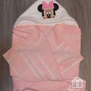 Op de afbeelding: Roze badcape met witte strepen en een witte kap met een geborduurd Minnie Mouse-ontwerp met een roze strik.