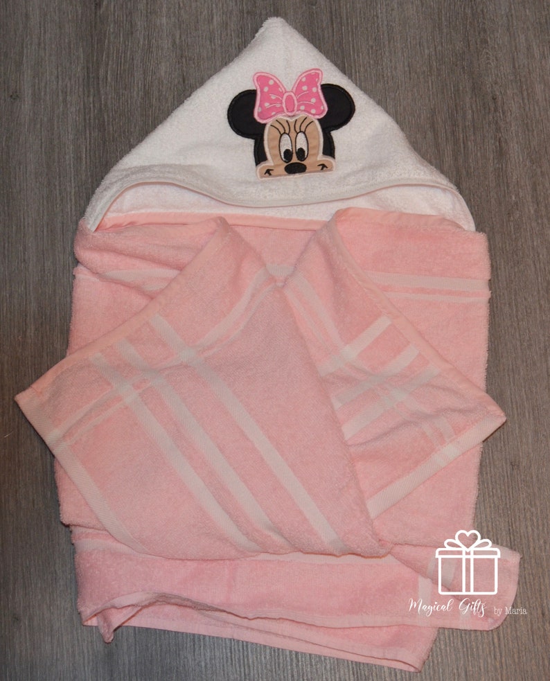 Op de afbeelding: Roze badcape met witte strepen en een witte kap met een geborduurd Minnie Mouse-ontwerp met een roze strik.