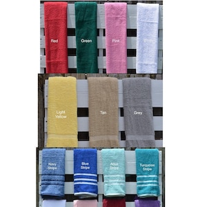 Op de afbeelding: Een selectie van handdoeken in kindermaten in verschillende kleuren en patronen. De handdoeken worden gepresenteerd op een wit houten pallet. De kleuren omvatten rood, groen, roze, wit, lichtgeel, bruin, grijs, donkerblauw met strepen, blauw met strepen, aquablauw met strepen, turquoise met strepen, wit met strepen, roze met strepen, rood met strepen en paars met strepen.