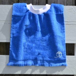 Op de afbeelding: Een blauwe badstof slabbetje met een witte rand en een witte geschenkdoos met een hartvormig ontwerp en de tekst "Magical Gifts".