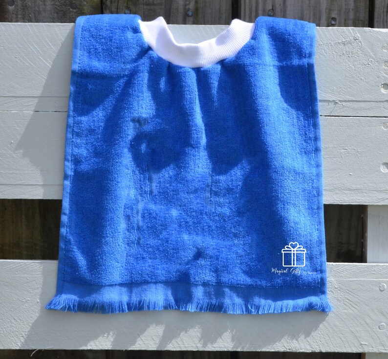 Op de afbeelding: Een blauwe badstof slabbetje met een witte rand en een witte geschenkdoos met een hartvormig ontwerp en de tekst "Magical Gifts".