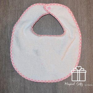 Op de afbeelding: Witte baby-slabbetje met een roze en witte geruite rand. Het slabbetje heeft een drukknoop sluiting aan de hals.