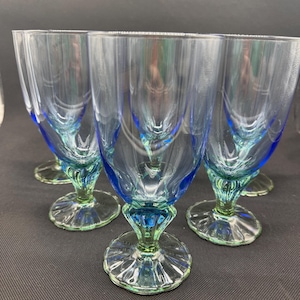 Könnte beinhalten: Set aus fünf transparenten Glasbechern mit blauen und grünen Akzenten. Die Stiele und Basen sind grün, während die Schalen einen blauen Farbton aufweisen. Die Becher haben ein strukturiertes Design.