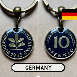 May include: A keychain with a German 10 Pfennig coin from 1993. The coin has a dark blue background with gold lettering and a gold oak leaf design. The word "GERMANY" is displayed below the coin.