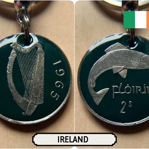 May include: A keychain with two sides of an Irish coin from 1965. One side shows a harp and the word "Éire". The other side displays a fish and the word "Flóirín". The coin is green with silver detailing.