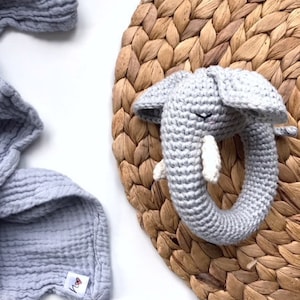 May include: A gray crocheted elephant rattle toy with a ring for a baby to hold. The toy is on a woven straw mat.