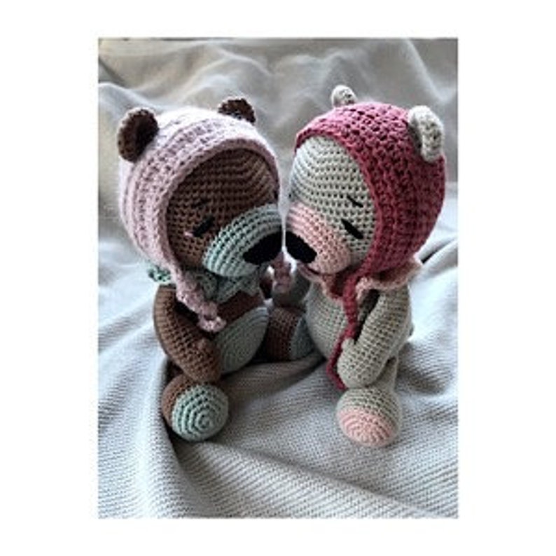 May include: Two crocheted teddy bears wearing pink and light blue hats. The bears are sitting next to each other and are both looking down.