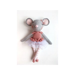 May include: A crocheted gray mouse wearing a pink and white ballerina dress with a white tulle skirt. The mouse has pink ears and a pink nose.