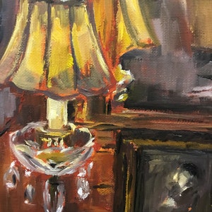 May include: A vintage-style table lamp with a yellow lampshade and a clear glass base with crystal accents. The lamp is sitting on a wooden table next to a framed picture.