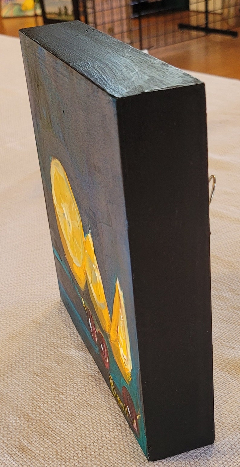 May include: A small, framed painting of a still life with lemons and red berries on a blue background. The painting is signed "Rigoni" in the lower right corner.