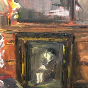 May include: A framed painting of a person sitting in a chair, with a dark brown frame and a gold inner frame. The painting is on a wooden shelf with a dark brown background.