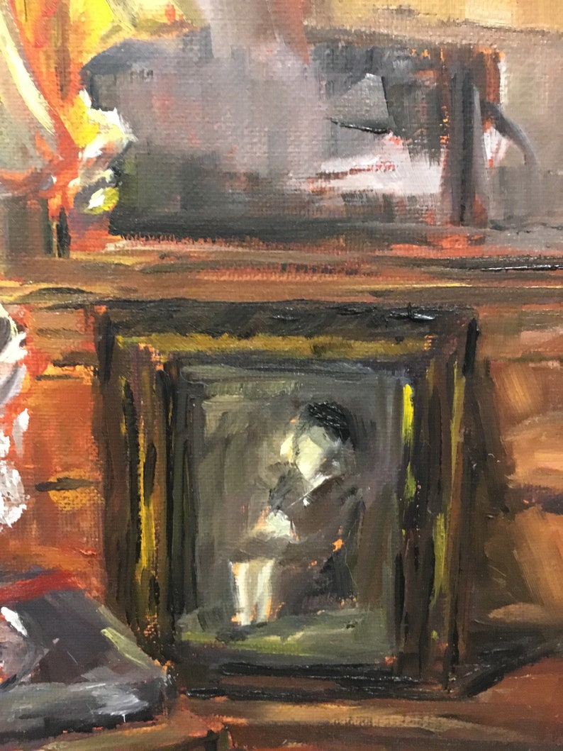 May include: A framed painting of a person sitting in a chair, with a dark brown frame and a gold inner frame. The painting is on a wooden shelf with a dark brown background.