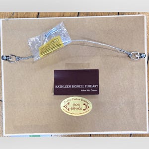 May include: The back of a framed artwork, showing the mounting hardware, wire, and labels. The labels include the artist's name, "Kathleen Bignell Fine Art," and the framer's information, "Corby Custom Framing."