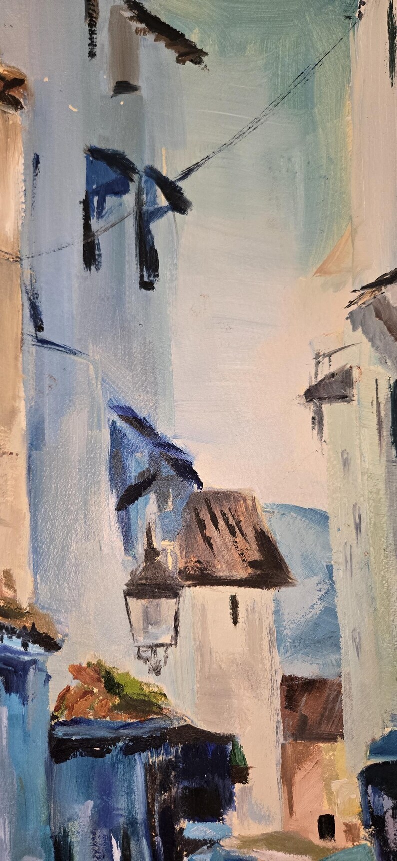 May include: An abstract oil painting depicting a European street scene. The artwork features buildings in shades of white, blue, and brown, with a street lamp and power lines. The brushstrokes are visible, creating a textured effect.
