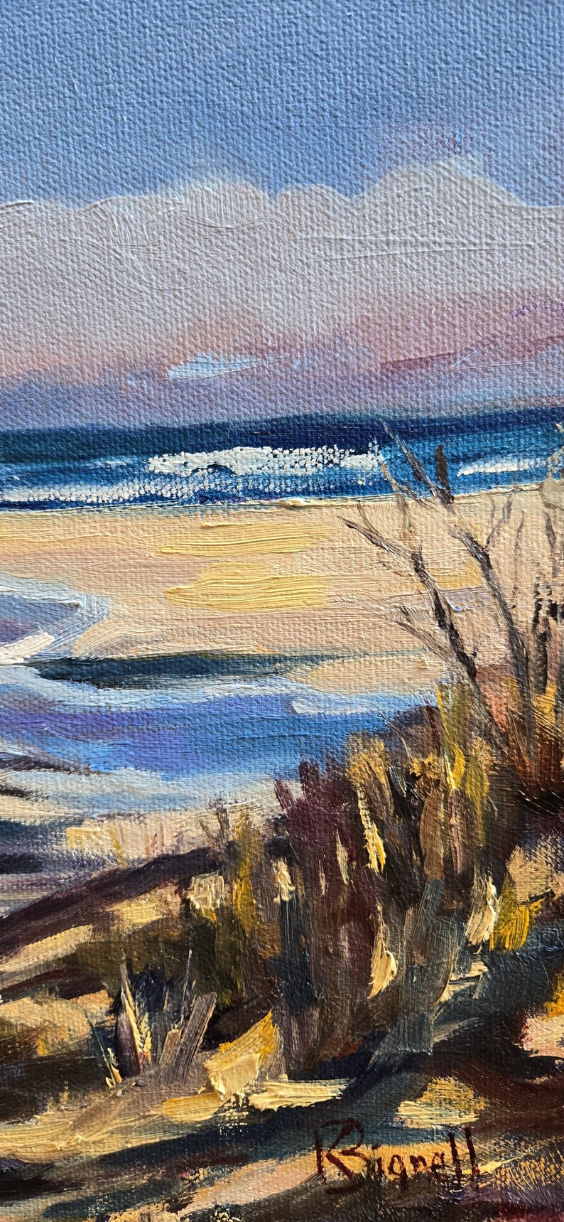 May include: A painting of a seascape with a sandy beach, blue water, and a cloudy sky. The painting is done in a loose, impressionistic style, with visible brushstrokes. The artist's signature, "Ruggell", is visible in the lower right corner.