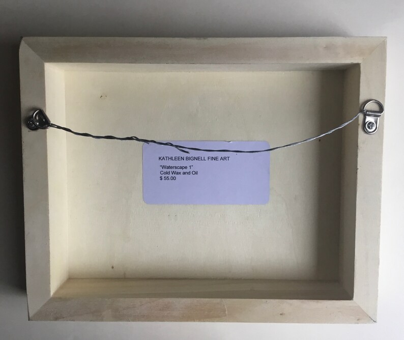 K&ouml;nnte beinhalten: Die R&uuml;ckseite eines gerahmten Gem&auml;ldes mit einem wei&szlig;en Passepartout und einem hellen Holzrahmen. Ein Drahtb&uuml;gel ist an der R&uuml;ckseite des Rahmens befestigt. Ein Etikett auf der R&uuml;ckseite des Rahmens lautet "KATHLEEN BIGNELL FINE ART" "Waterscape 1" Kaltwachs und &Ouml;l 55,00 &euro;