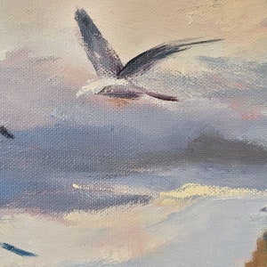 Op de afbeelding: Een olieverfschilderij dat een kustlandschap weergeeft met een bewolkte lucht en een vliegende zeemeeuw. Het kunstwerk heeft een gedempt kleurenpalet met tinten blauw, grijs en perzik. Het schilderij vangt een serene, natuurlijke omgeving.