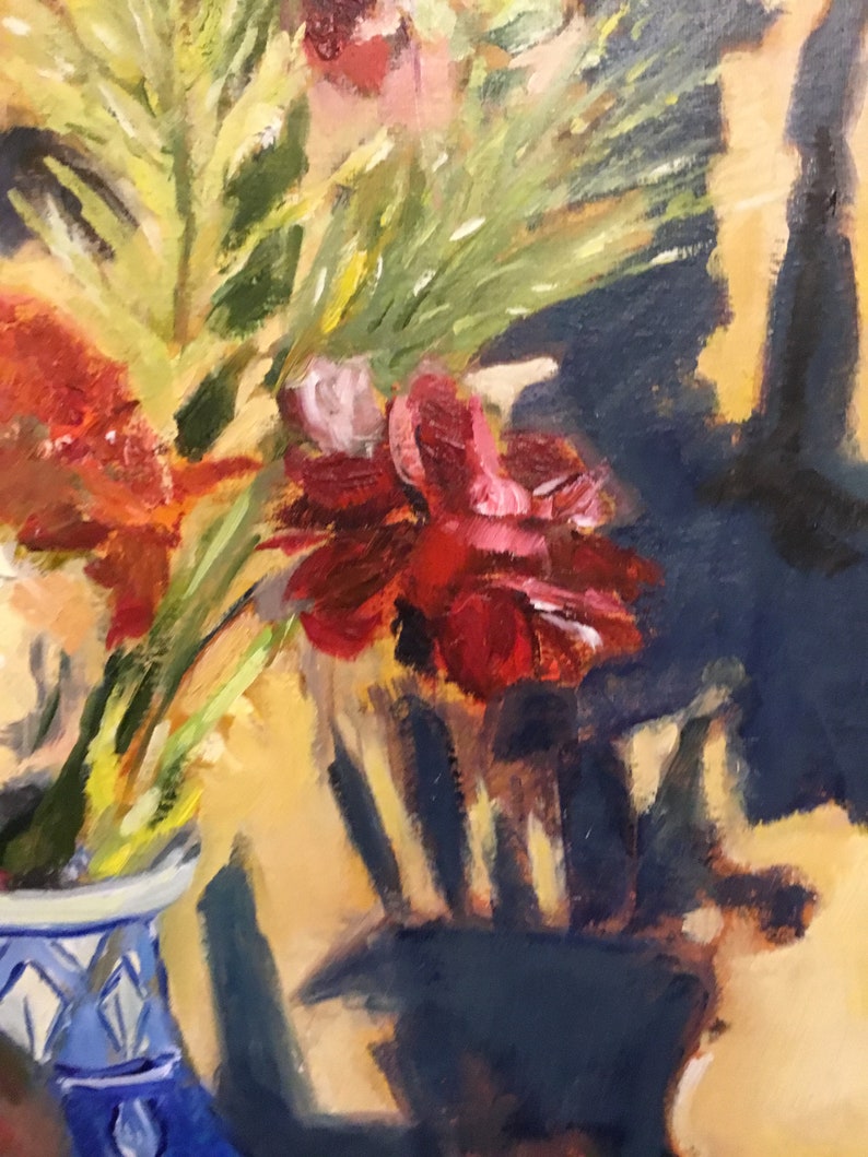 May include: A close-up of a bouquet of red, orange, and pink flowers in a blue and white vase. The flowers are arranged in a vase with a geometric pattern. The background is a blurred image of a dark blue wall.