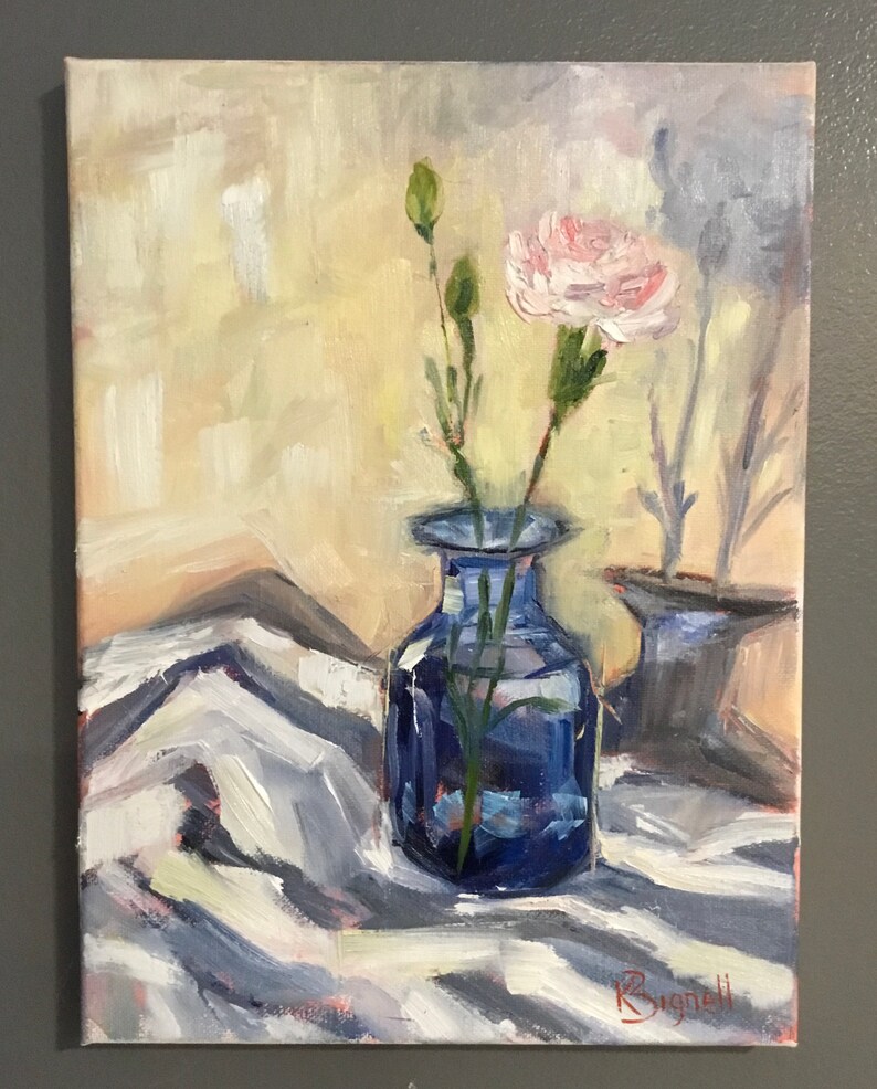 May include: An oil painting depicts a still life with a blue vase holding a pink carnation and green stems. The vase sits on a white and gray patterned cloth. A second blue vase is in the background. The background is a light yellow.