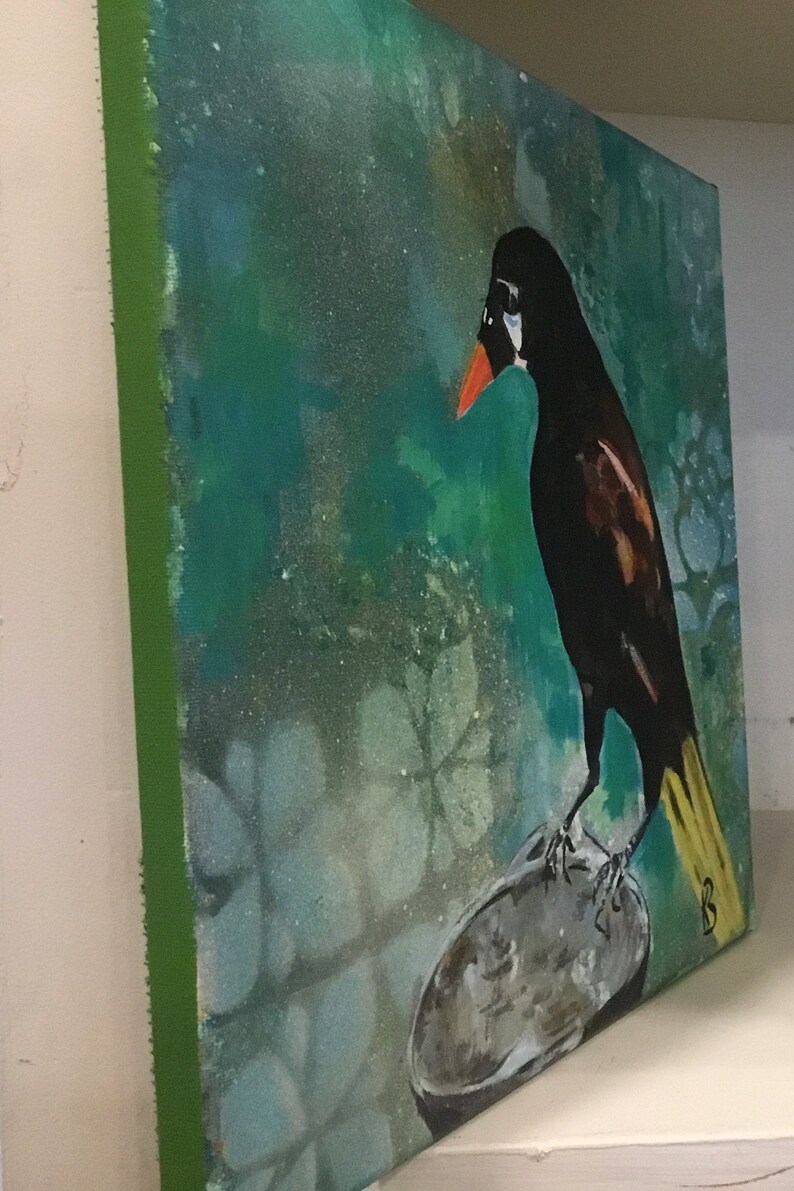Op de afbeelding: Een schilderij van een zwarte vogel met een gele staart die op een grijze rots zit. De achtergrond is turquoise groen met een wit bloemenpatroon.