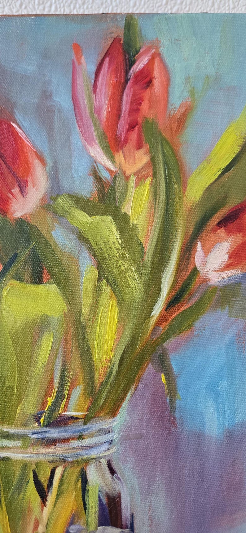Puede incluir: Pintura al &oacute;leo de tulipanes rojos en un jarr&oacute;n de cristal. Las flores tienen p&eacute;talos rojos vibrantes con toques de rosa y amarillo, y hojas verdes. El fondo es una mezcla de tonos azules y morados, creando una sensaci&oacute;n art&iacute;stica suave.