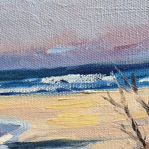 May include: A painting of a seascape with a blue sky, blue water, and a sandy beach. The water is choppy and there are whitecaps on the waves. The beach is empty and there are some trees in the background.