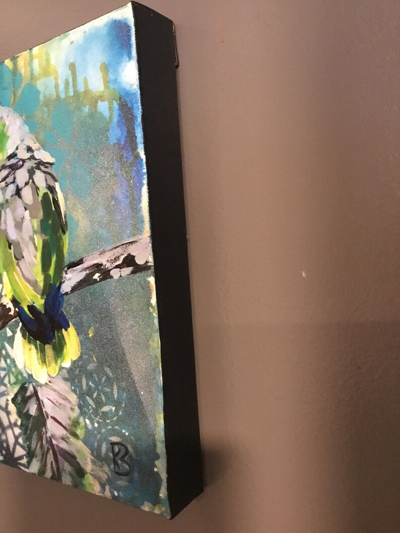 Puede incluir: Una pintura de un loro verde y blanco posado en una rama. El fondo es un dise&ntilde;o abstracto azul y verde con acentos blancos. La pintura est&aacute; enmarcada con un marco negro.