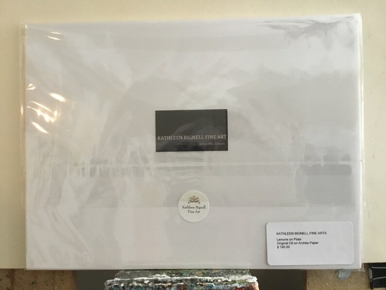May include: A white envelope with a black label that reads "KATHLEEN BIGNELL FINE ART" and a smaller white label with the text "KATHLEEN BIGNELL FINE ARTS" and the words "Lemons on Plate, Original Oil on Arches Paper, $100.00".