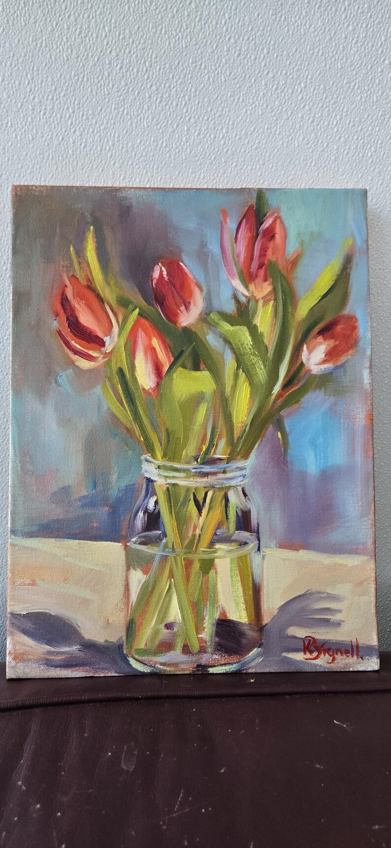 Puede incluir: Pintura al &oacute;leo de un ramo de tulipanes rojos en un tarro de cristal transparente. Los tulipanes tienen tallos y hojas verdes. El fondo es una mezcla de azul, morado y blanco. La pintura est&aacute; firmada en la esquina inferior derecha.