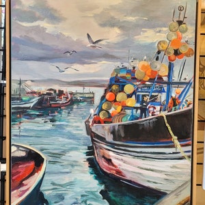 Op de afbeelding: Olieverfschilderij van een haven met vissersboten. Het kunstwerk toont een donkere boot met oranje en gele boeien, zeemeeuwen en een bewolkte lucht. Het schilderij is ingelijst in een licht houten frame.