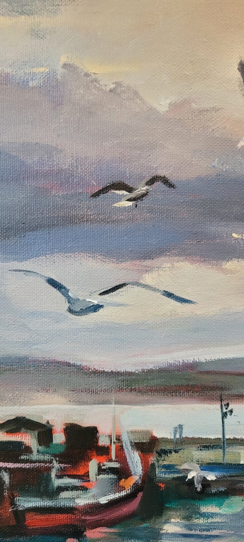 Op de afbeelding: Olieverfschilderij van een kustlandschap met vliegende zeemeeuwen. Het kunstwerk toont een haven met boten en gebouwen onder een bewolkte hemel. Het kleurenpalet omvat tinten blauw, grijs, rood en wit, wat een serene sfeer cre&euml;ert.
