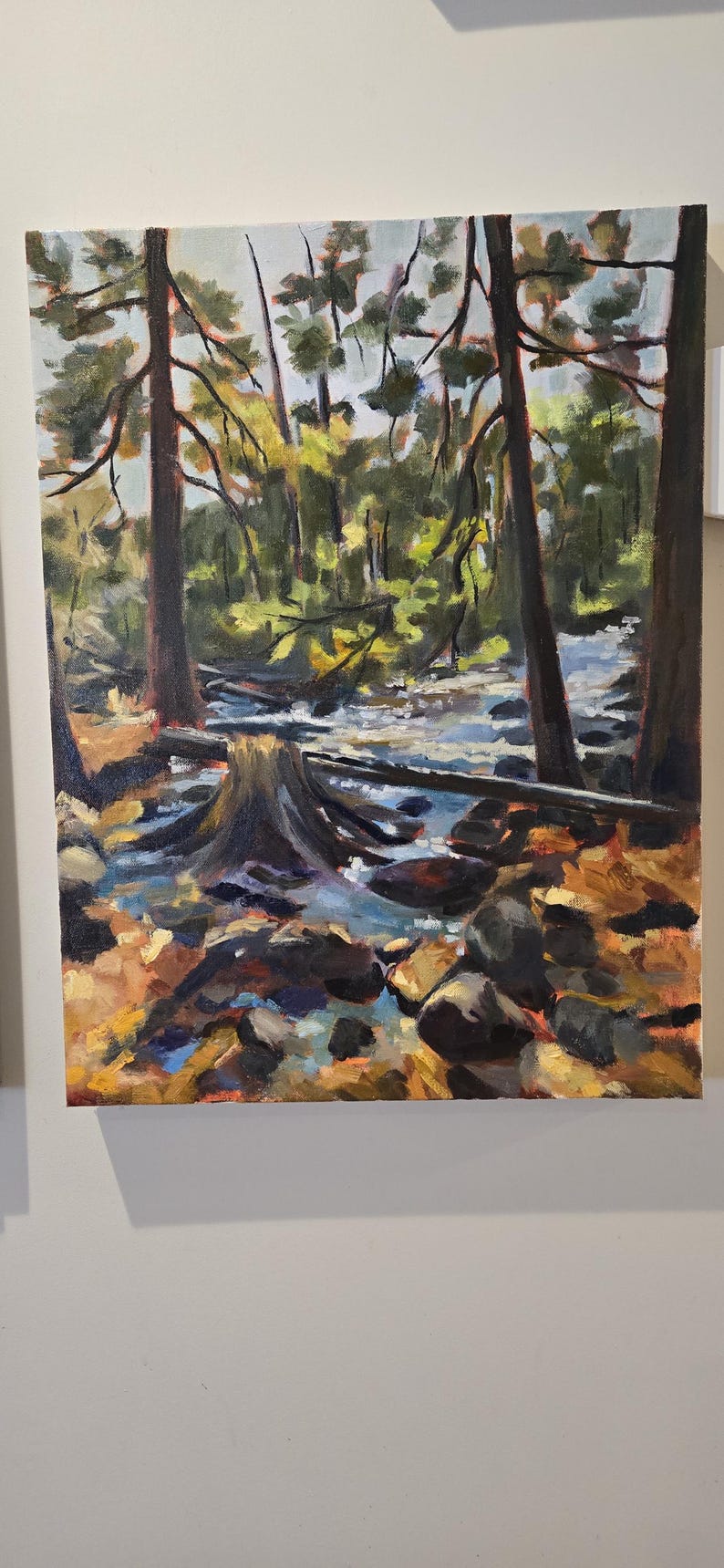 May include: Oil painting of a forest scene with a stream. The artwork features tall trees with brown trunks and green foliage. The stream has blue and white reflections, and the foreground has rocks and fallen leaves.