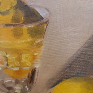 Op de afbeelding: Olieverfschilderij van een stilleven met een kristallen glas gevuld met een gele vloeistof. Het glas heeft een decoratief patroon. Een gele vrucht is gedeeltelijk zichtbaar aan de rechterkant. De achtergrond is neutraal beige.