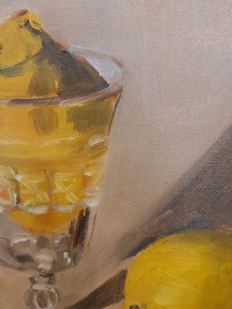 Op de afbeelding: Olieverfschilderij van een stilleven met een kristallen glas gevuld met een gele vloeistof. Het glas heeft een decoratief patroon. Een gele vrucht is gedeeltelijk zichtbaar aan de rechterkant. De achtergrond is neutraal beige.