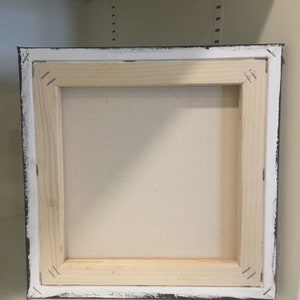 May include: The back of a stretched canvas painting with a wooden frame. The canvas is white and the frame is painted black with white edges.