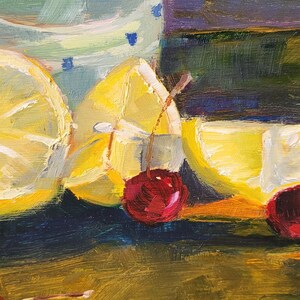 Puede incluir: Pintura de naturaleza muerta con limones cortados y cerezas. Los limones son de un amarillo brillante, y las cerezas son de un rojo intenso. Un vaso con un patr&oacute;n azul y blanco es parcialmente visible en el fondo. La pintura tiene un ambiente c&aacute;lido y acogedor.