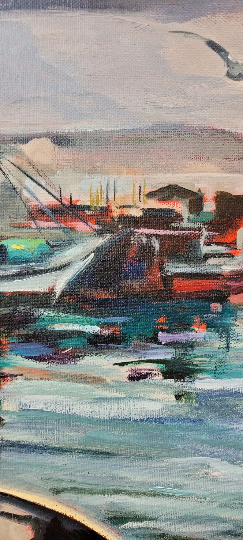 Op de afbeelding: Een abstract olieverfschilderij van een havengezicht. Het kunstwerk toont een zeemeeuw in de lucht, boten en gebouwen met een palet van blauw, groen, rood en bruin. Het water weerspiegelt de kleuren van de lucht en de gebouwen.