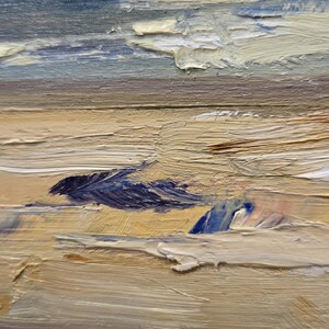 May include: An oil painting on canvas depicting a coastal landscape with thick, textured impasto brushstrokes. The scene features a sandy beach in shades of beige and tan, transitioning into blue ocean waves and a soft, pale yellow and blue sky.