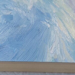 May include: A close-up of a blue and white abstract painting with visible brushstrokes. The painting is framed and the frame is a light wood color.