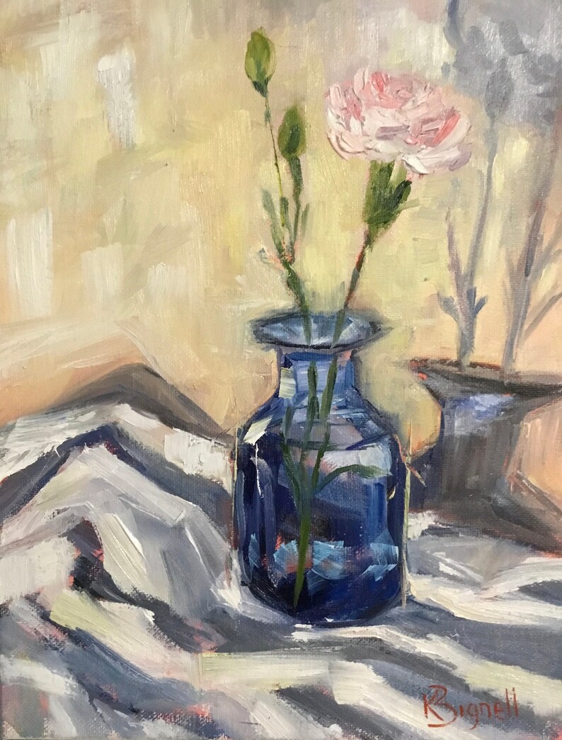 May include: An oil painting depicts a blue glass vase holding a pink carnation and green buds. The vase sits on a white and gray striped cloth. The background is a soft yellow and peach color. The artist's signature, Bignell, is in the lower right corner.