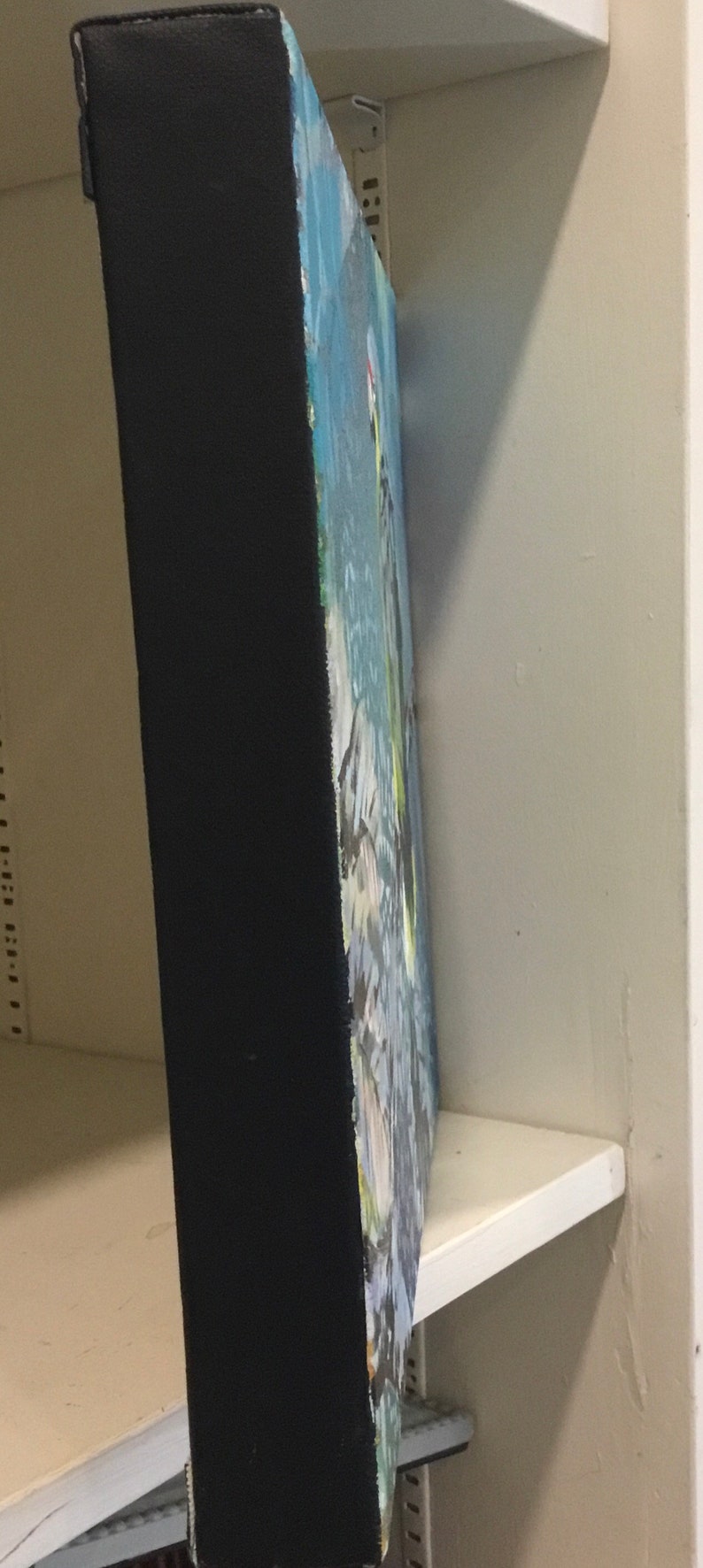 Puede incluir: Una pintura enmarcada con un marco negro y un dise&ntilde;o abstracto colorido. La pintura est&aacute; colgada en un estante blanco.