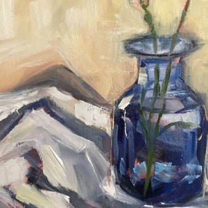 May include: An oil painting depicts a cobalt blue glass vase holding slender green stems. The vase sits on a white and gray cloth, with a soft, beige background. The artwork uses visible brushstrokes.