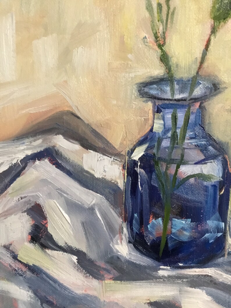 May include: An oil painting depicts a cobalt blue glass vase holding slender green stems. The vase sits on a white and gray cloth, with a soft, beige background. The artwork uses visible brushstrokes.