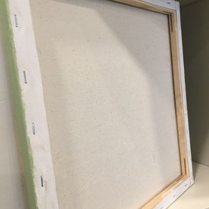 May include: A square, stretched canvas art panel with a light beige surface. The canvas is stapled to a wooden frame. The edges of the canvas are wrapped around the frame and secured with staples. The frame is white with a light green edge.