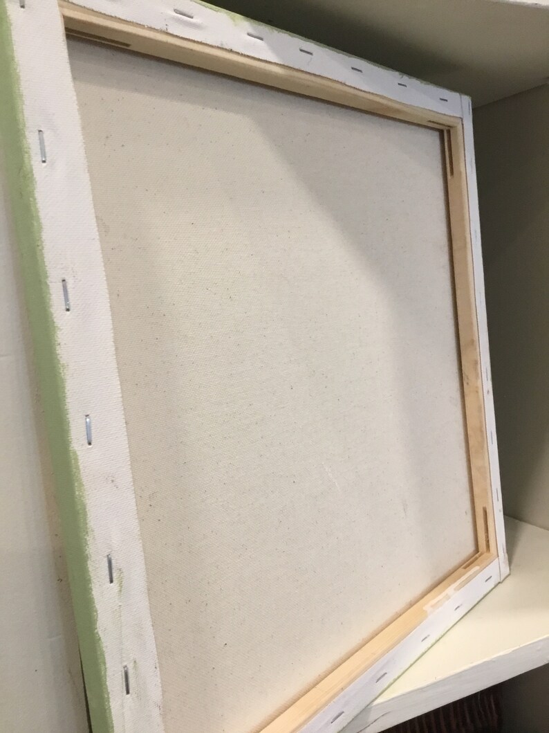May include: A square, stretched canvas art panel with a light beige surface. The canvas is stapled to a wooden frame. The edges of the canvas are wrapped around the frame and secured with staples. The frame is white with a light green edge.
