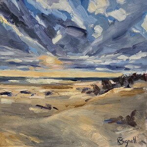 May include: An oil painting on canvas depicting a coastal landscape at sunset. The scene features a sandy beach in the foreground with textured brushstrokes in shades of beige and brown, leading to a dark ocean horizon under a dramatic sky filled with thick, layered clouds in shades of deep blue, grey, and white. The artist's signature, Bignell, is visible in the bottom right corner.