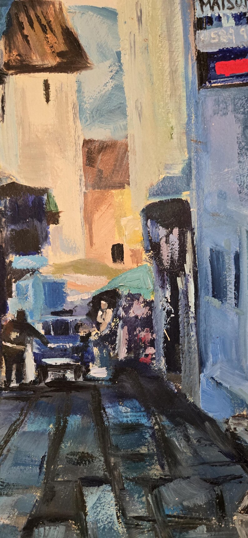 May include: An impressionistic oil painting of a European street scene. Buildings in shades of blue, beige, and brown line the street. Figures are suggested in the foreground, with a shop sign visible in the background.