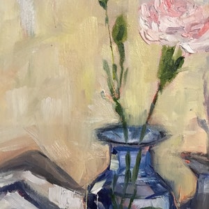 May include: An oil painting of a blue glass vase holding a pink carnation and two green buds. The background is a soft blend of yellow and white, with visible brushstrokes. A white and gray patterned cloth is visible in the lower left corner.