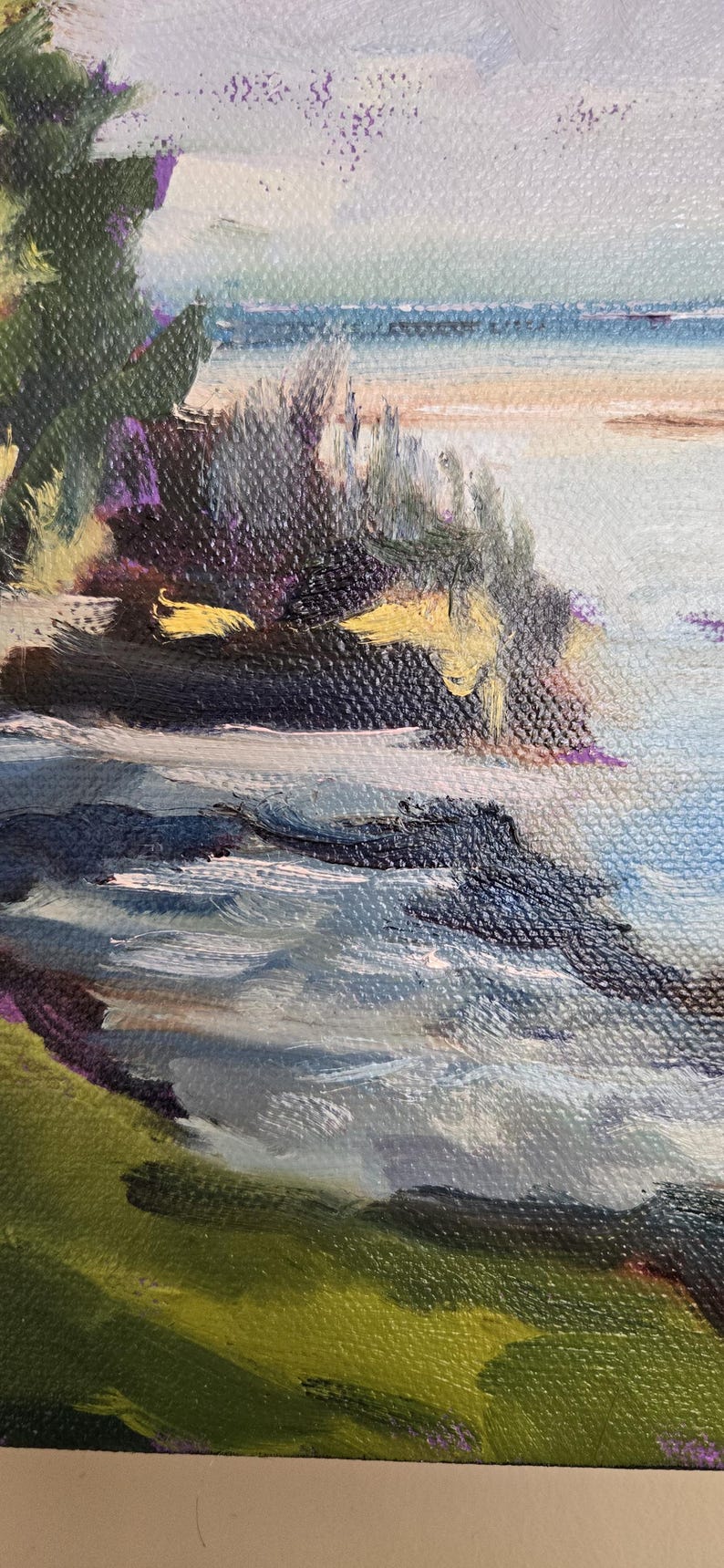 May include: A painting of a seascape with a rocky shoreline and a blue sky with white clouds. The water is a light blue and the rocks are a dark gray. The sky is a light blue with white clouds.